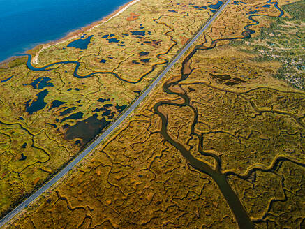 Aerial shot of expansive marshlands with meandering rivers, pools, and a distant road bordering the coastline - ADSF49062
