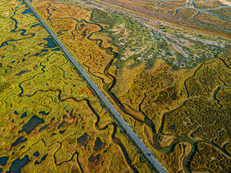 Aerial shot of expansive marshlands with meandering rivers, pools, and a distant road bordering the coastline - ADSF49063