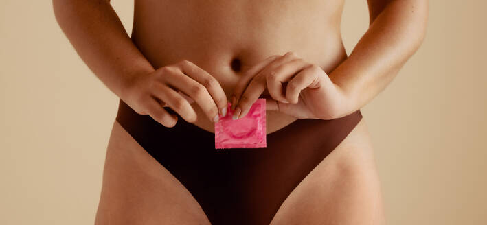 Eine selbstbewusste Frau, die ein Kondom in der Hand hält und für geschützten und sicheren Sex wirbt. Diese fesselnde Studioaufnahme ermutigt zu einem positiven Umgang mit sexuellem Wohlbefinden zwischen Mann und Frau. - JLPPF02382