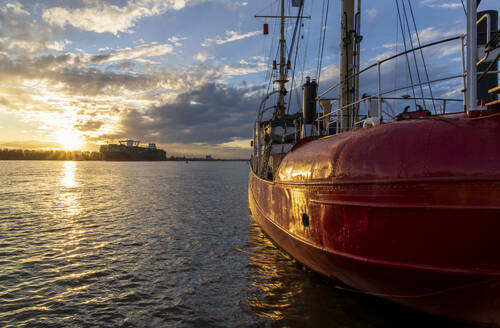Deutschland, Hamburg, Elbe 3 Schiff bei Sonnenuntergang mit Hamburger Hafen im Hintergrund - IHF01844
