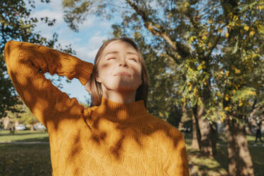 Woman with eyes closed enjoying sunlight at autumn park - OSF02326