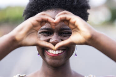 Smiling young woman gesturing heart shape - WPEF07803