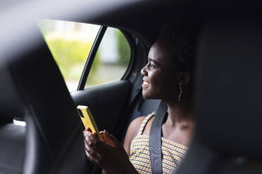 Lächelnde junge Frau mit Smartphone im Auto - WPEF07810