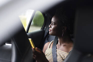 Nachdenkliche junge Frau mit Smartphone im Auto - WPEF07811