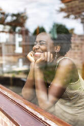 Glückliche junge Frau, die sich auf einen Ellbogen stützt, durch ein Fenster gesehen - WPEF07824