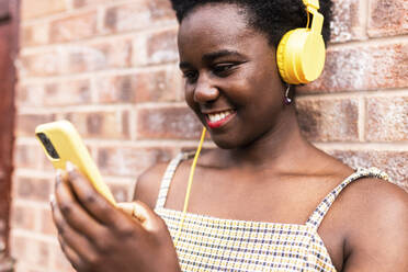 Lächelnde Frau, die ein Smartphone benutzt und vor einer Mauer Musik hört - WPEF07826