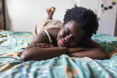 Smiling woman resting on bed in bedroom - WPEF07838