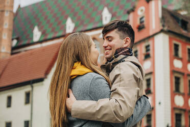 Happy man embracing girlfriend in front of building - VSNF01438