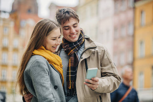 Lächelnder Mann teilt Smartphone mit Freundin auf der Straße - VSNF01442