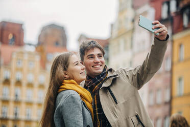 Happy man taking selfie with girlfriend through smart phone at street - VSNF01443