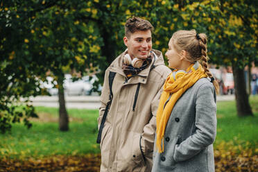 Smiling man looking at girlfriend walking with hand in pocket at street - VSNF01453