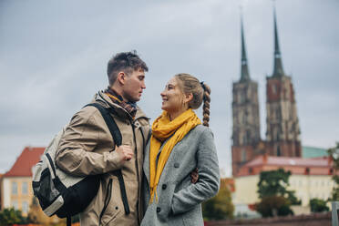 Romantic man with arm around girlfriend standing in front of building - VSNF01454