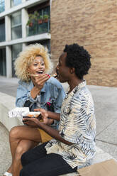 Transgender woman feeding sushi to boyfriend sitting on bench - VRAF00256