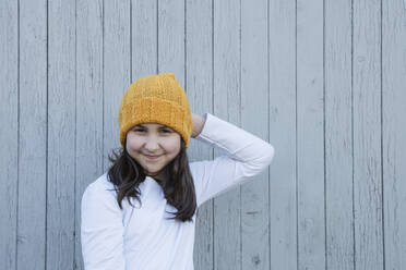 Lächelndes Mädchen mit gelber Strickmütze vor einer Holzwand - OSF02335
