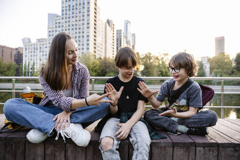 Happy mother playing with sons sitting on bench - EYAF02869