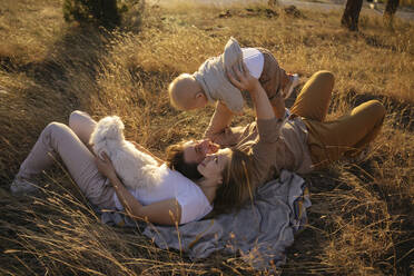 Parents spending leisure time with son and dog lying down at field - YBF00309