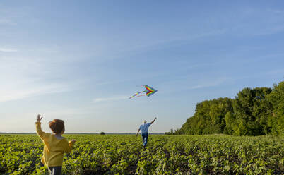 Grandfather and grandson flying kite in agricultural field under sky - MBLF00165