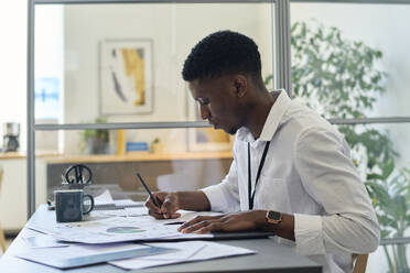 Junger Geschäftsmann bei der Arbeit an Diagrammen und Tabellen im Büro - DSHF01095