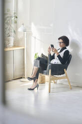 Young businesswoman sitting in chair and using mobile phone - DSHF01105