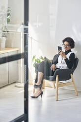 Young businesswoman using smart phone and sitting in chair - DSHF01106