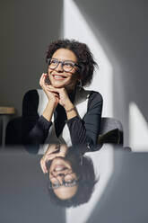 Happy businesswoman wearing eyeglasses sitting at desk in office - DSHF01113