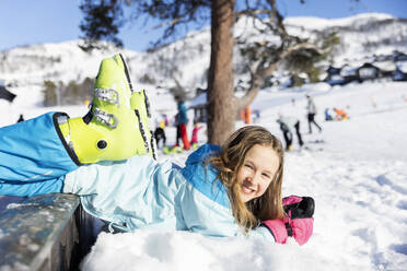 Smiling girl lying in snow on mountain - FOLF12337