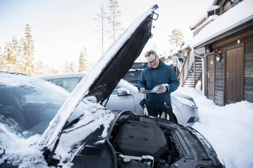 Man looking at manual while repairing car - FOLF12353