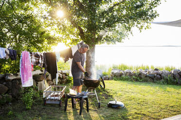 Man cooking on barbecue by sea at sunset - FOLF12390