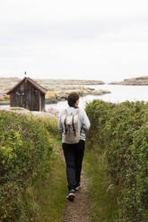 Woman walking to cabin by coast - FOLF12401