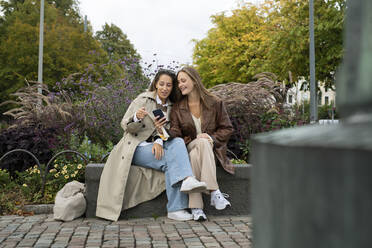 Junge Frauen sitzen auf einer Bank im Park - FOLF12485