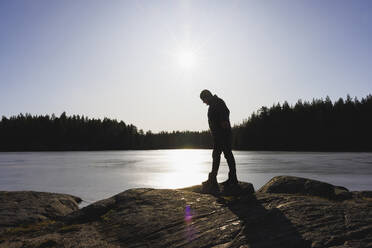 Man walking on rocks by lake at sunset - FOLF12513