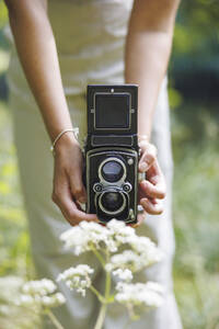 Young woman using vintage camera to photograph flowers - FOLF12526