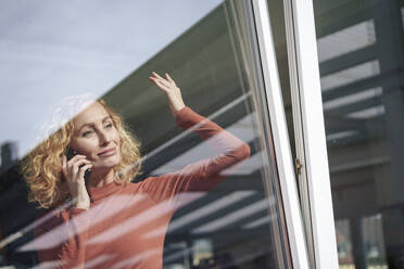 Smiling businesswoman talking on smart phone seen through glass - JOSEF22061