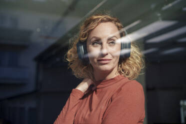 Woman wearing wireless headphones seen through glass - JOSEF22064