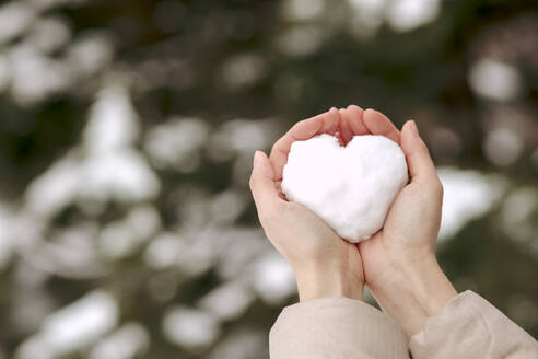 Woman holding heart shaped snow in cupped hands - VIVF01252