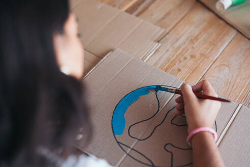 Close-up of a young woman's hands as she paints an earth design on cardboard, symbolizing environmental awareness and care. - ADSF49086