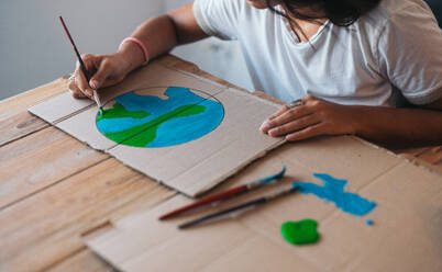 Close-up of a young woman's hands as she paints an earth design on cardboard, symbolizing environmental awareness and care. - ADSF49091