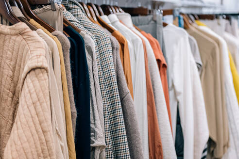 Close-up view of a variety of shirts, jackets and sweaters hung on wooden hangers in a store display. - ADSF49151