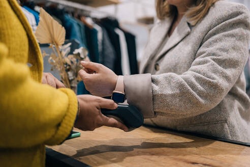 Close-up of a customer making a contactless payment to a store owner using a smartwatch. - ADSF49152