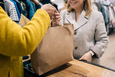 Close-up view of store owner caucasian female hands over a shopping bag to a customer at the checkout counter. - ADSF49153