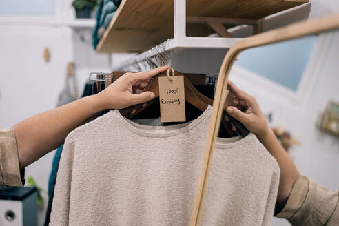 A second hand sweater on a wooden hanger with a cardboard tag in a store. - ADSF49157