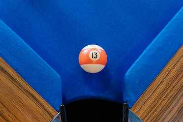 Top view of orange and white billiard ball on blue pool table near pocket - ADSF49161