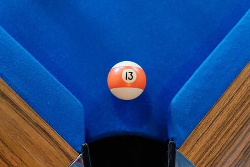 Top view of orange and white billiard ball on blue pool table near pocket - ADSF49161