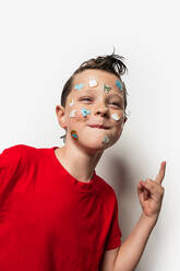 A young boy with wet hair has colorful animal stickers on his face, wearing a red shirt against a white background. - ADSF49166