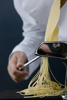 Close up of a chef hand turning the handle of a pasta maker with tagliolini coming out - FSIF06660