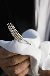 Nahaufnahme eines Kellners, der mit einer weißen Serviette eine silberne Gabel poliert - FSIF06661