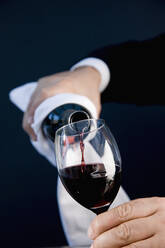 Nahaufnahme eines Kellners, der eine Flasche in den Händen hält und Rotwein in ein Glas gießt - FSIF06664