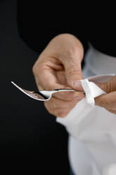 Nahaufnahme eines Kellners, der mit einer weißen Serviette eine silberne Gabel poliert - FSIF06665