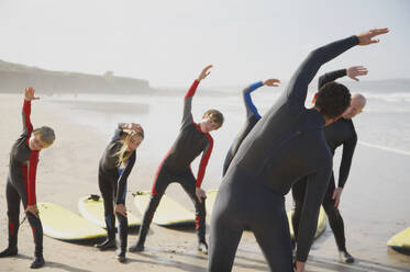 Rückenansicht eines Surflehrers und einer Gruppe von Schülern, die sich am Strand dehnen - FSIF06674