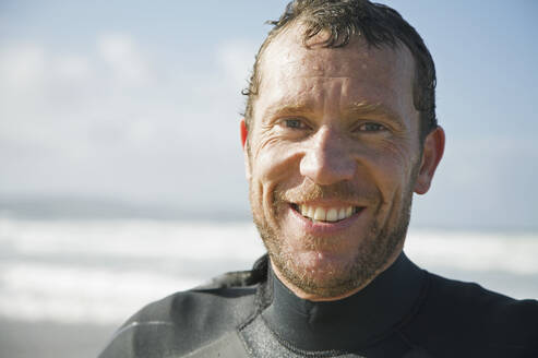 Smiling surfer standing on a beach - FSIF06678